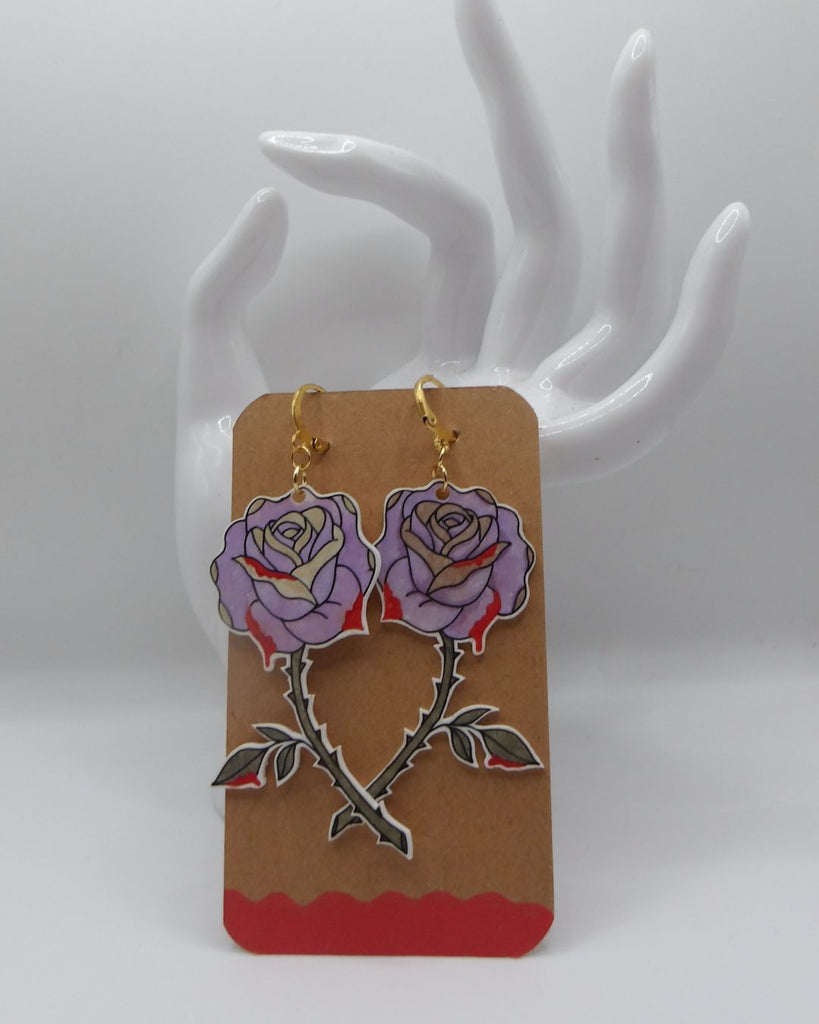 Foto van een paar oorbellen in halloween thema.  De oorbellen hebben goudkleurige hardware, en een tekening van prikende roze rozen. 