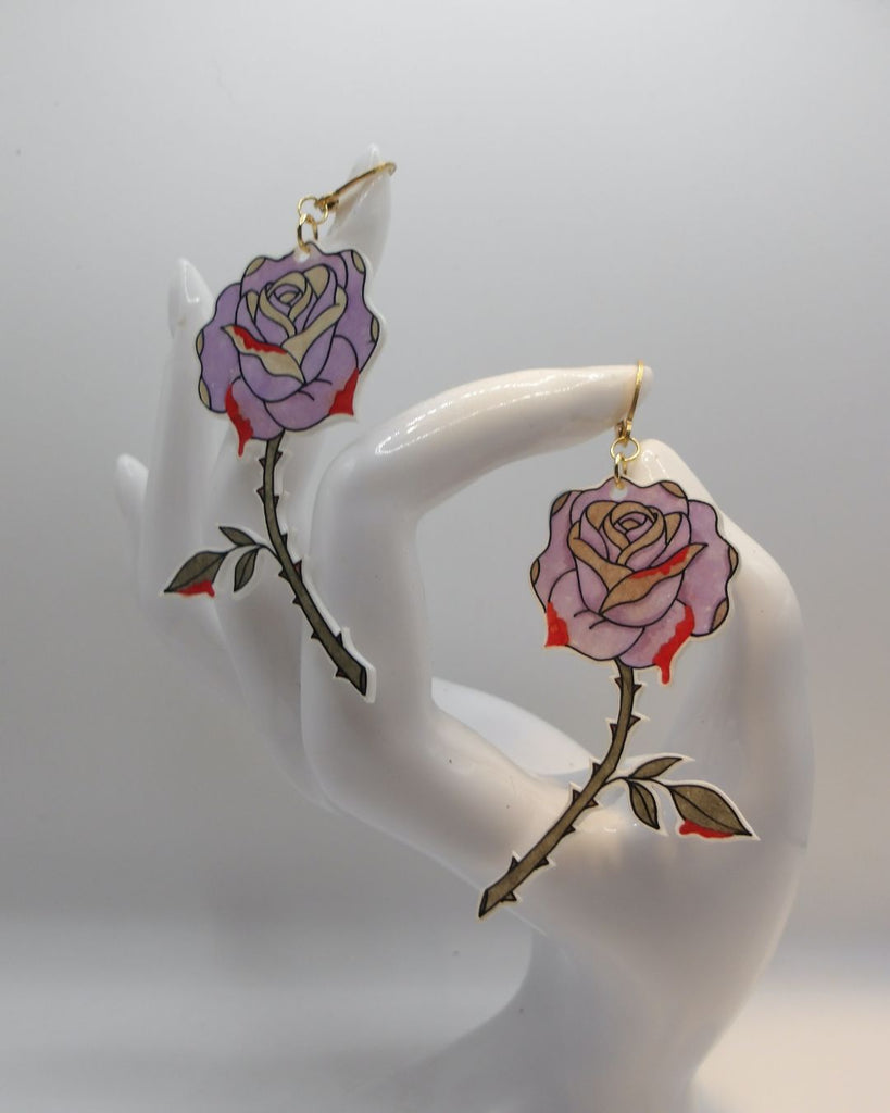 Foto van een paar oorbellen in halloween thema.  De oorbellen hebben goudkleurige hardware, en een tekening van prikende roze rozen. 