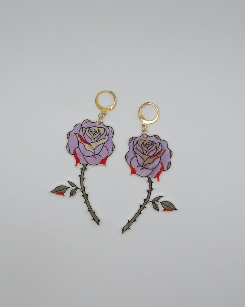 Foto van een paar oorbellen in halloween thema.  De oorbellen hebben goudkleurige hardware, en een tekening van prikende roze rozen. 