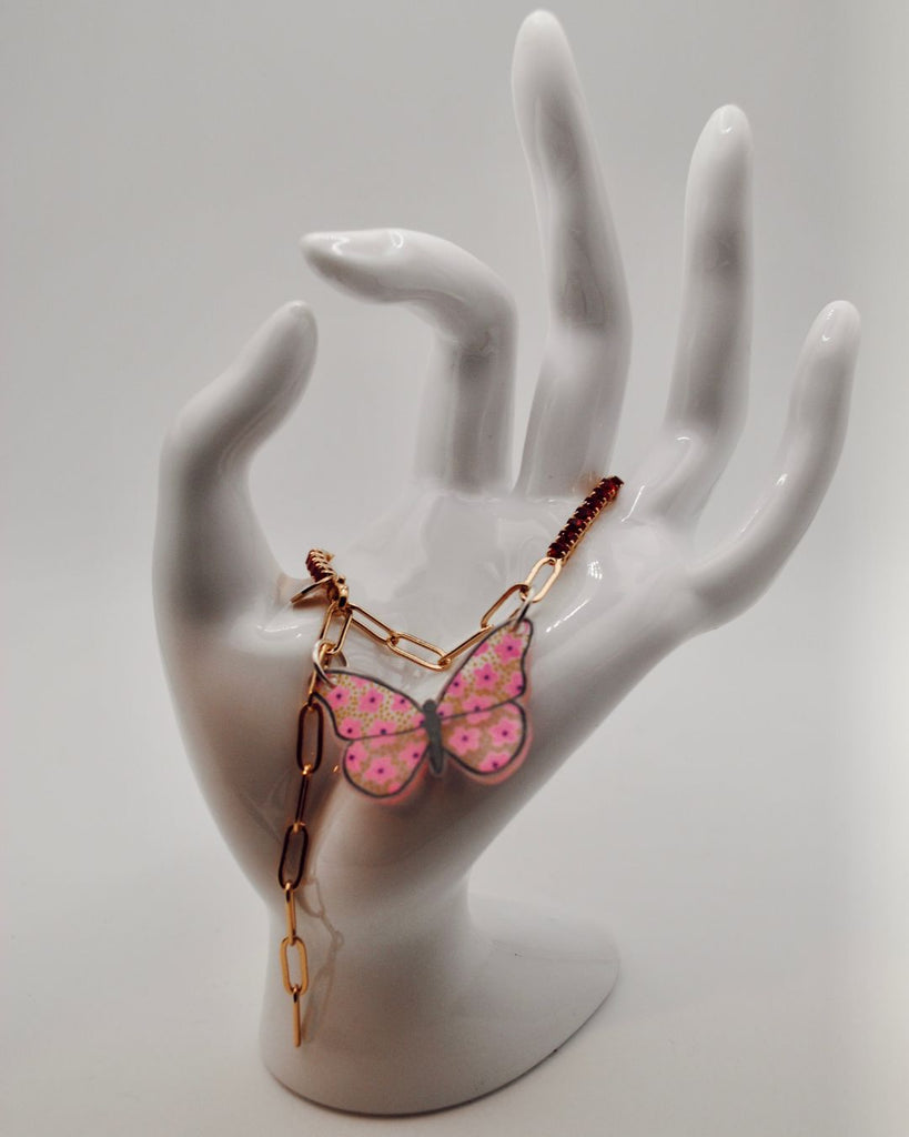 Foto van armbandje met rode steentjes en roze vlinder in krimpfolie, gedrapeerd over een witte hand