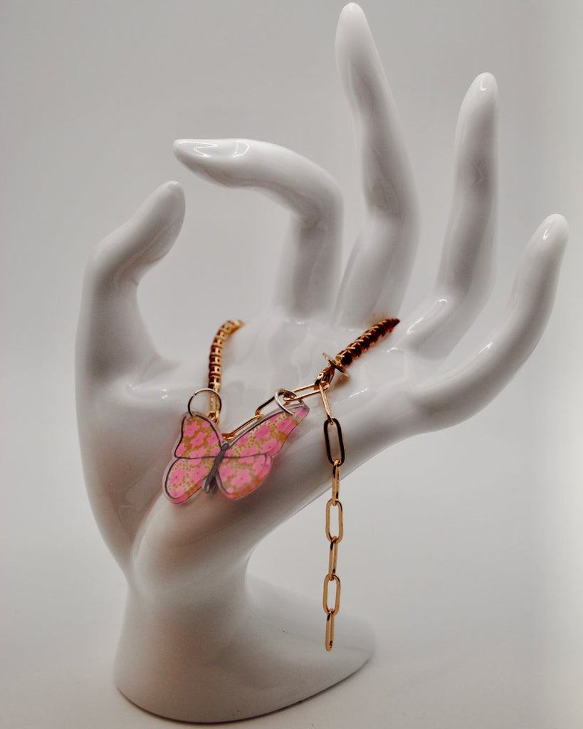 Foto van armbandje met rode steentjes en roze vlinder in krimpfolie, gedrapeerd over een witte hand
