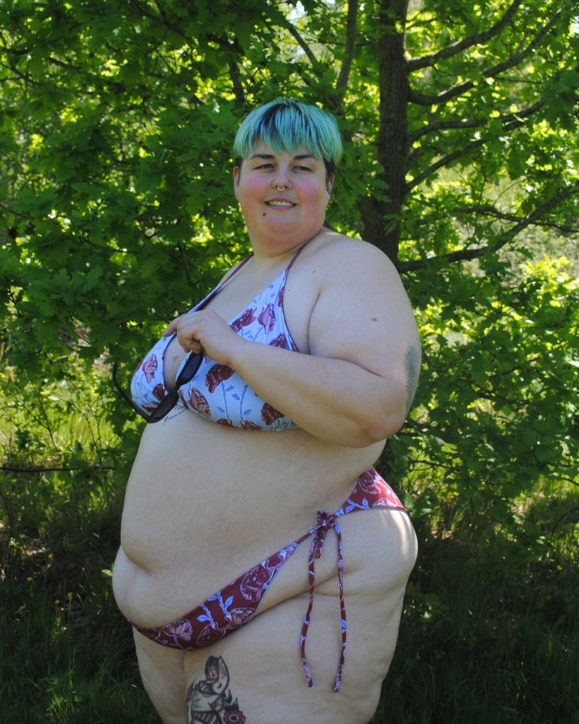 Achteraanzicht. Het model draagt een mismatch bikini top en broekje. De bikini heeft een bloemenprint. Het topje is helder blauw en het broekje is bordeaux.