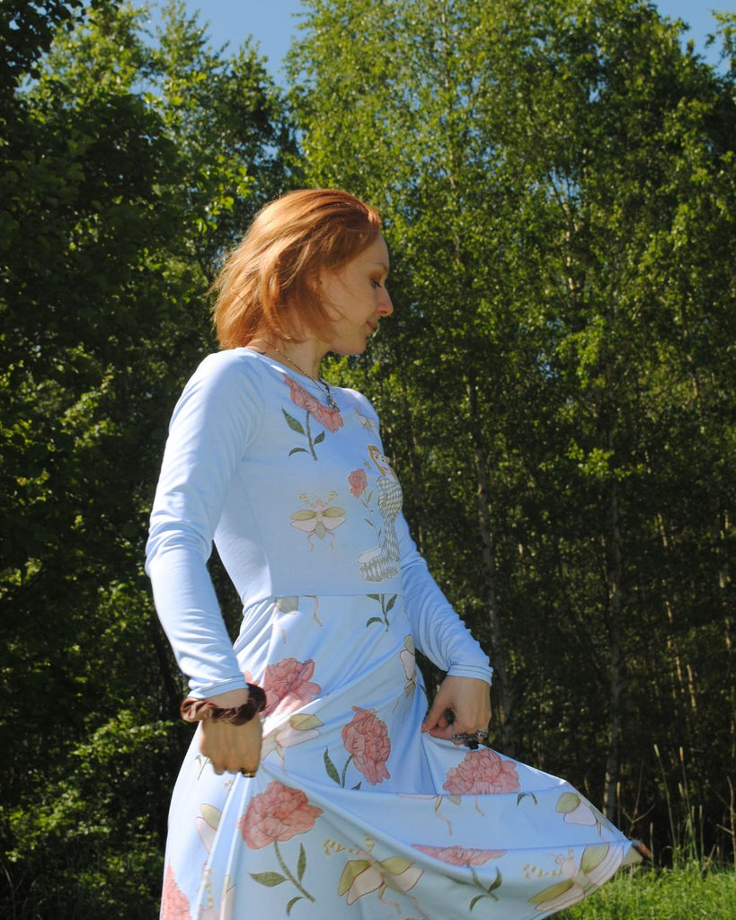 Het model draait met het zomers blauw jurkje . Het zwierige jurkje komt tot onder de knie. Het heeft een bloemenprint met een meisje dat tussen de bloemetjes zit. 