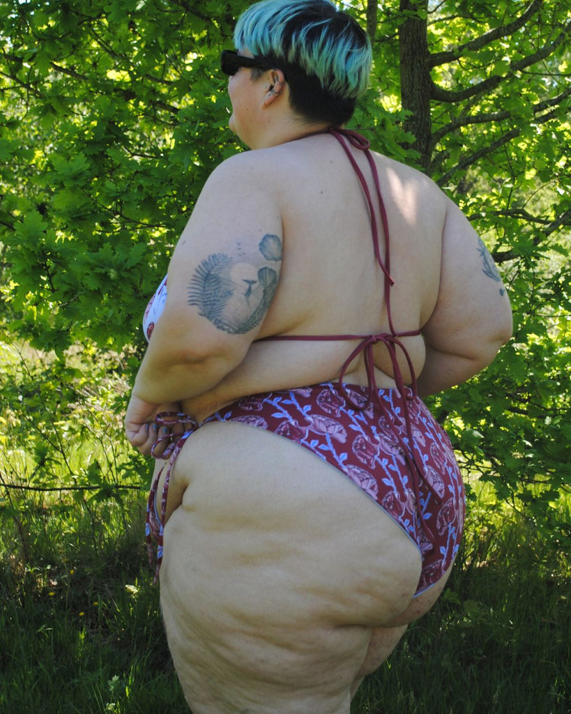 Achteraanzicht van de koordbikini. Het broekje is donkerrood en heeft een speelse bloemenprint in roze, blauw en bordeaux
