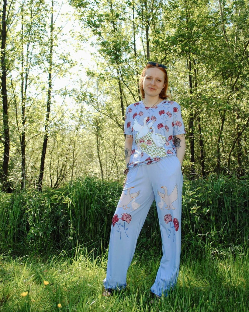 Model draagt matching blauwe set met een t-shirt en bijpassende broek met rechte pijpen. De broek heeft een unieke floral print met ganzen.