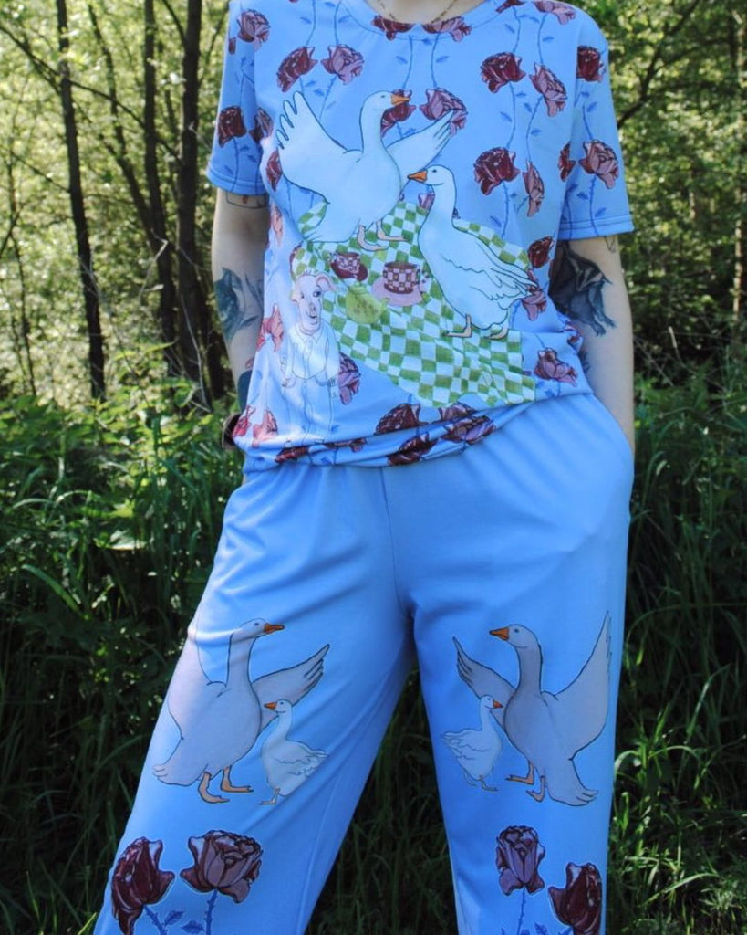 Model draagt matching blauwe set met een t-shirt en bijpassende broek met rechte pijpen. De broek heeft een unieke floral print met ganzen.