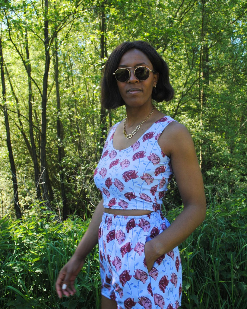 Zijaanzicht. Het vrouwelijke model draagt een matching set met een crop top en short in blauw met bloemenprint in roze, bordeaux en blauw. 