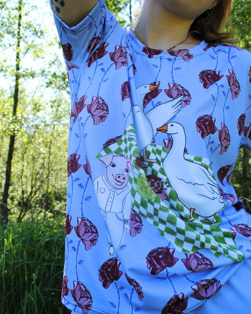 Originele blauwe t-shirt met bloemenprint en een picknick tafereel met ganzen en een biggetje. 