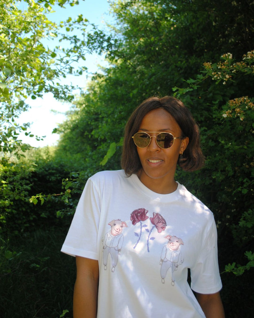 Vooraanzicht. Model draagt witte t-shirt met illustratieve print van 2 biggetjes en bloemetjes.