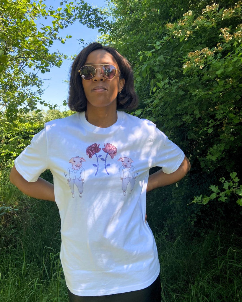Vooraanzicht. Model draagt witte t-shirt met illustratieve print van 2 biggetjes en bloemetjes.